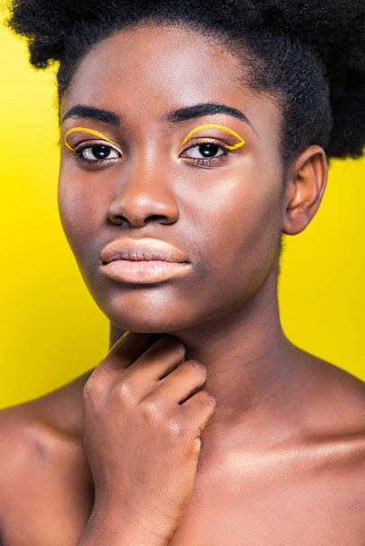 Attractive african american woman with trendy makeup looking at camera isolated on yellow - Photo, Image
