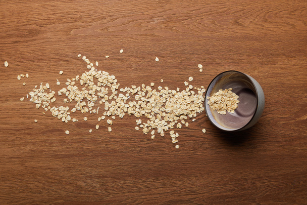 top view of oat flakes scattered near bowl at wooden table  - Foto, imagen