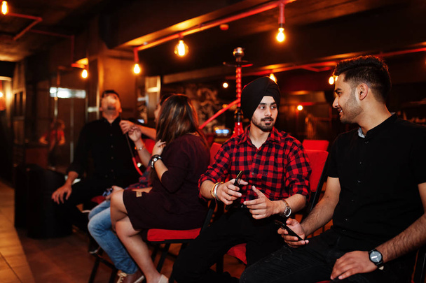 Group of indian friends sitting at lounge bar, smoke hookah and  - Photo, Image