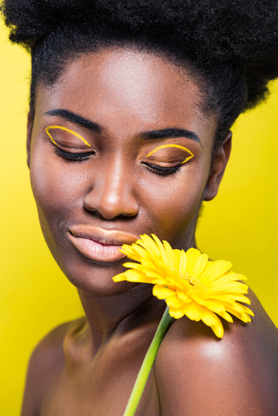 schöne afrikanisch-amerikanische Frau mit geschlossenen Augen hält Blume isoliert auf gelb - Foto, Bild