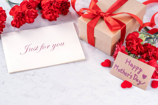 May mothers day handmade giftbox wishes photography - Beautiful blooming carnations with red ribbon bow box isolated on modern marble desk, close up, copy space, mock up - Photo, image