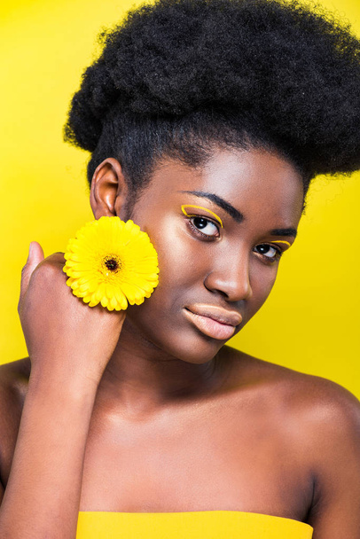 Grave menina americana africana com flor olhando para a câmera isolada no amarelo
 - Foto, Imagem