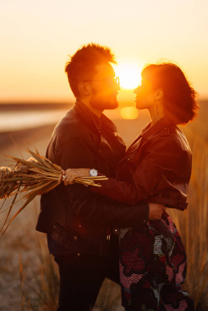 Enjoying time together.  Stylish and loving couple enjoying each other by the sea. The couple is young and in love. The concept of youth, love and lifestyle. Beautiful sunset on a summer day. - Fotografie, Obrázek