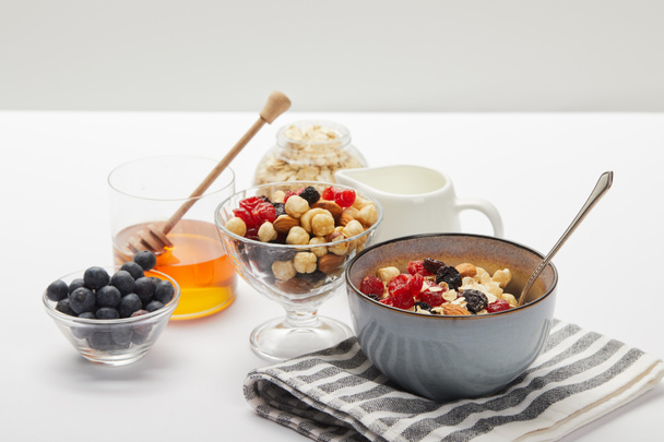 мюсли с ягодами, орехами и медом на завтрак на белом столе, изолированном на сером
 - Фото, изображение