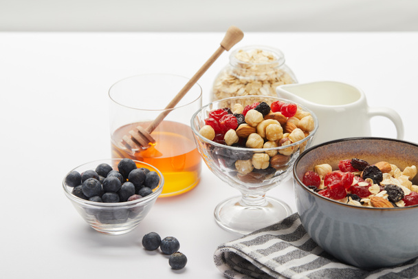 muesli with berries, nuts and honey in bowls served for nutritious breakfast on white table isolated on grey - Photo, Image