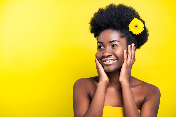 Cheerful smiling african american woman with flower on yellow - Фото, зображення