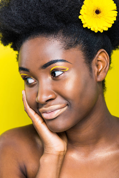 Dreamy african american woman with flower in hair looking away isolated on yellow - Photo, Image