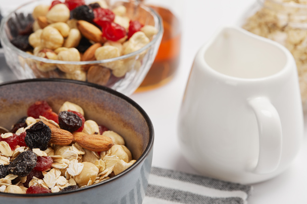 selective focus of bowl on striped napkin with oat flakes, nuts and berries near milk jug - Fotografie, Obrázek