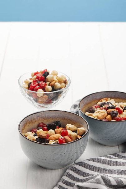 bowls with muesli, dried berries and nuts served for breakfast isolated on blue - 写真・画像