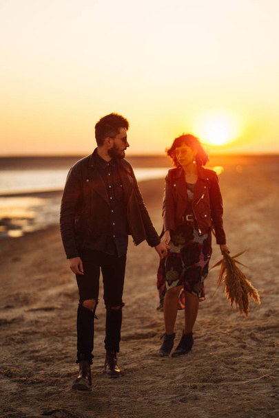 Enjoying time together.  Stylish and loving couple enjoying each other by the sea. The couple is young and in love. The concept of youth, love and lifestyle. Beautiful sunset on a summer day. - Foto, Imagen