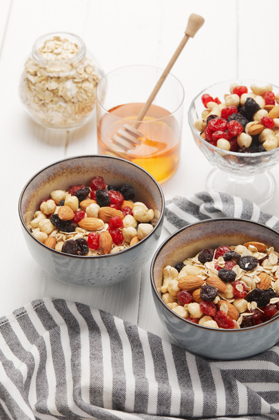 bowls with muesli, dried berries and nuts served for breakfast with honey on white wooden table - Foto, Bild