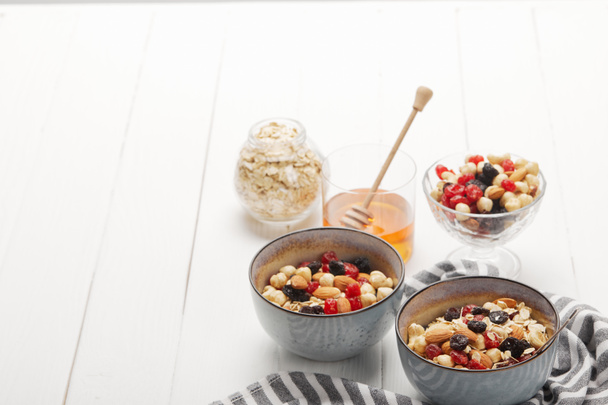 bowls with muesli, dried berries and nuts served for breakfast with honey on white wooden table with copy space - Foto, Imagem