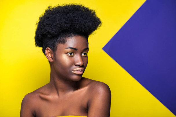 Мечтательная африканская американка смотрит в сторону желтого и фиолетового
 - Фото, изображение