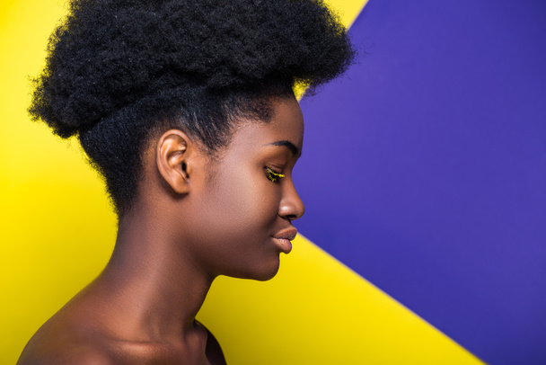 Vista lateral de la encantadora mujer afroamericana en amarillo y púrpura
 - Foto, Imagen