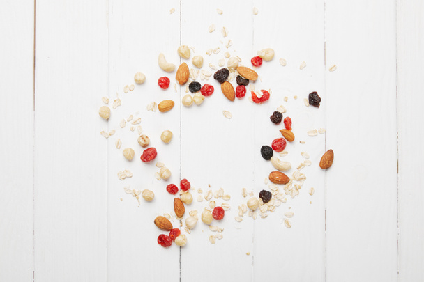 top view of scattered dried berries, oat flakes and nuts on white wooden table - 写真・画像