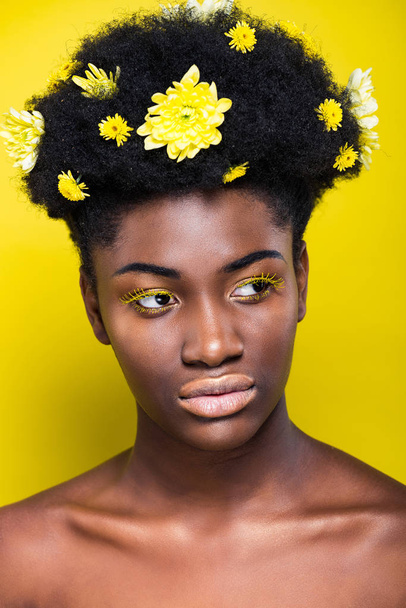 Ragazza afroamericana pensierosa con i fiori nei capelli guardando altrove sul giallo
 - Foto, immagini