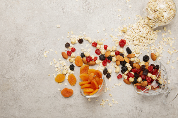 top view of oat flakes, dried apricots and berries, nuts messy scattered on textured grey surface  - Fotografie, Obrázek