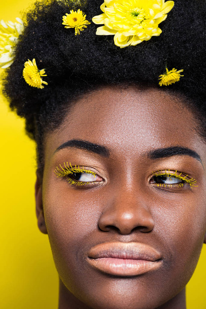 Retrato de mujer afroamericana con flores en pelo sobre amarillo
 - Foto, Imagen