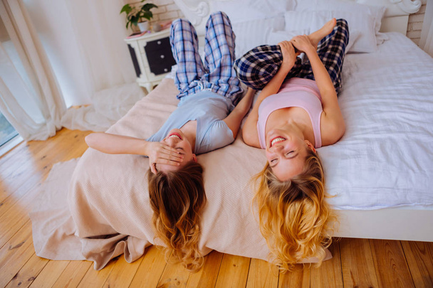 Funny sisters laughing after joking while lying on bed - Photo, Image