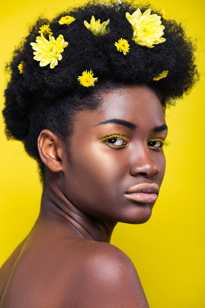 Beautiful african american woman with chrysanthemums in hair isolated on yellow - Foto, afbeelding