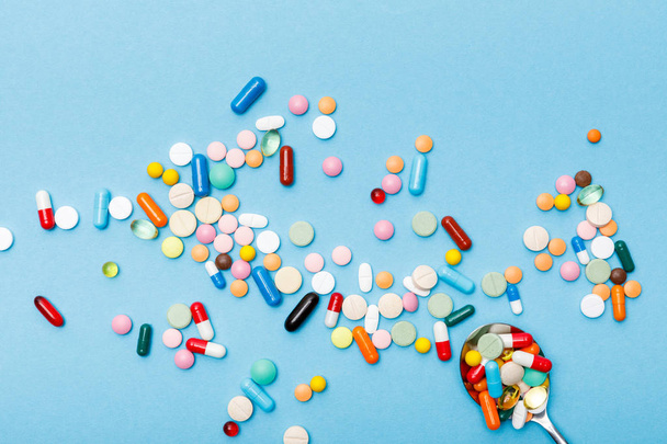 Top view of colorful pills and spoon on blue surface - Fotó, kép