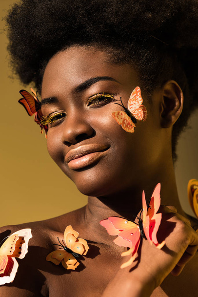 Smiling african american woman with butterflies isolated on brown - Photo, Image