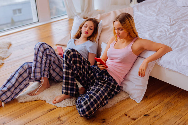 Δύο αδελφές, χρησιμοποιώντας το smartphone τους κάθεται στο πάτωμα κοντά στο κρεβάτι - Φωτογραφία, εικόνα