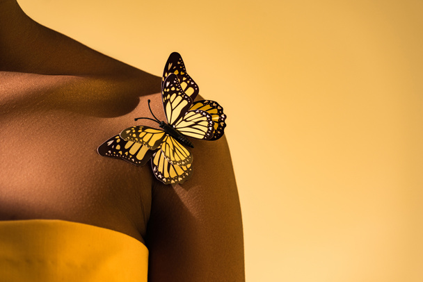 Cropped view of african american woman with butterfly on shoulder on orange - Фото, изображение