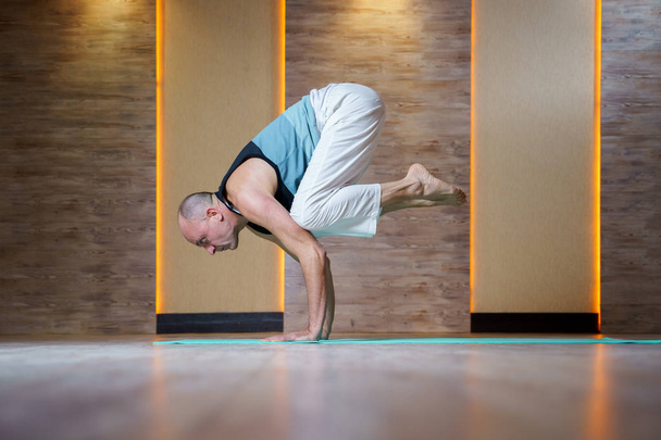 Sportive man practices yoga while standing on hands on blue mat. - Fotó, kép