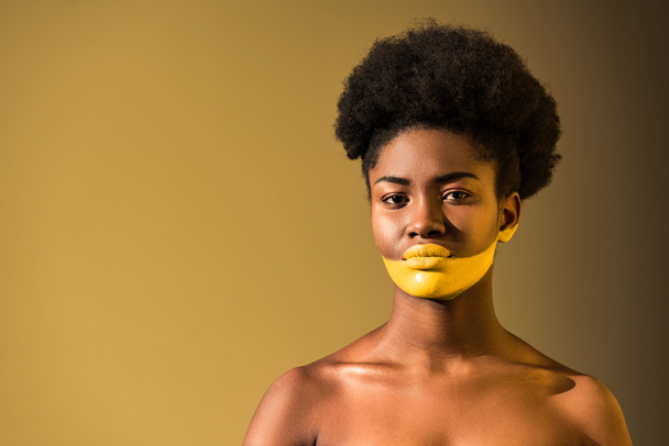 Serious african american woman with yellow body art on brown - Фото, зображення