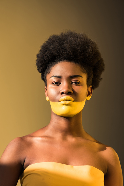 Serious african american woman with yellow body art on brown - Foto, imagen
