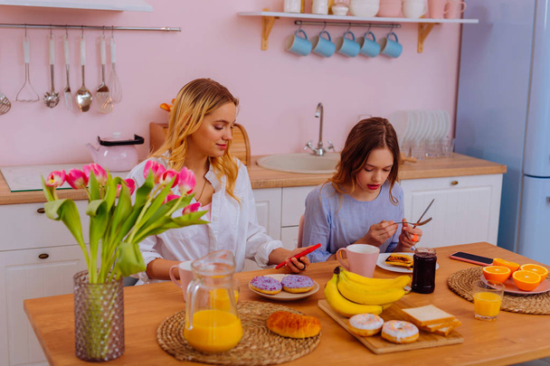 Sisters enjoying breakfast at home eating some doughnuts - Foto, Imagen