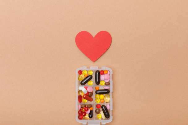 Top view of container with pills and paper heart on brown surface - Photo, Image