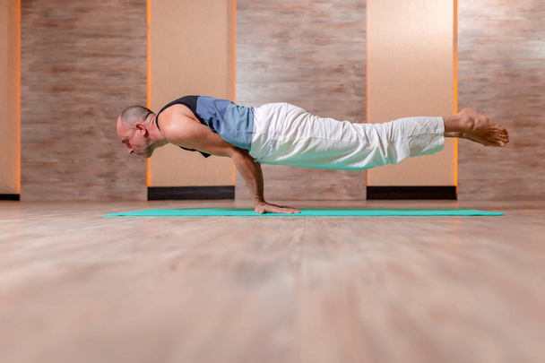 Adult athlete man practices yoga while standing on hands on blue mat. - Фото, зображення