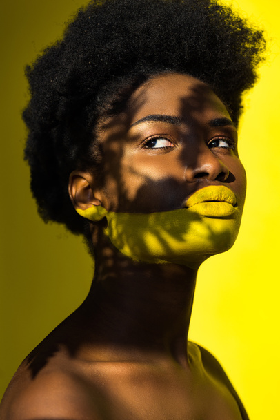Мечтательный молодой африканский американец с искусством тела смотрит в сторону желтого
 - Фото, изображение