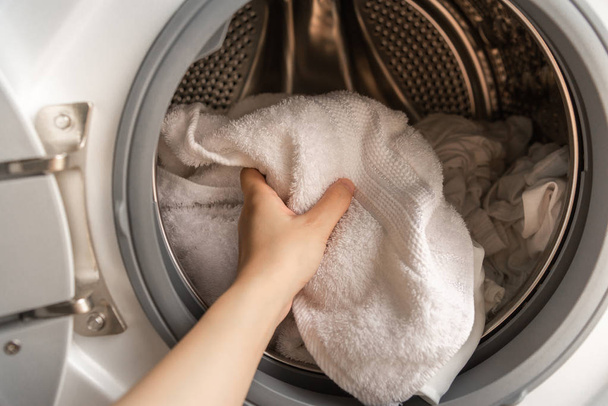 Close up van vrouw linkerhand witte handdoeken laden in een wasmachine. - Foto, afbeelding