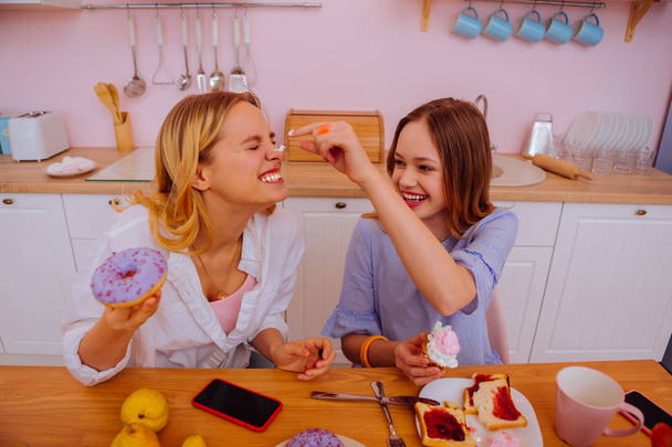 Girl having fun putting some whipped cream on nose of sister - 写真・画像