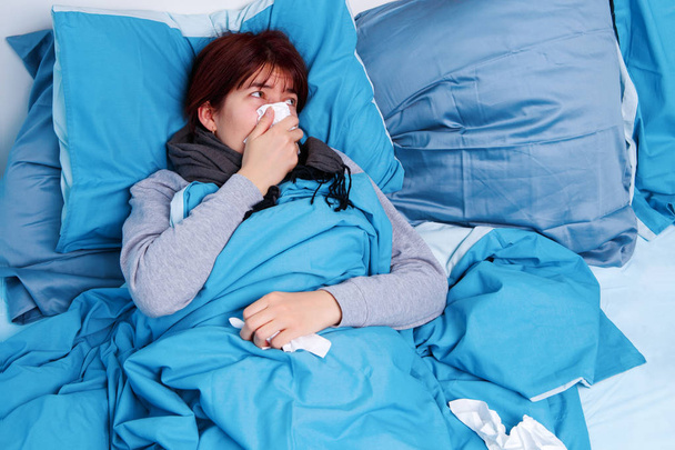 Foto di una bruna malata che si soffia il naso nel fazzoletto di carta sdraiata a letto
 - Foto, immagini