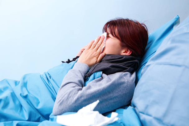 Photo of sick brunette blowing her nose in paper handkerchief lying in bed - 写真・画像