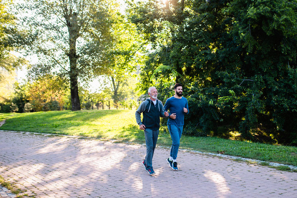 Happy father and son jogging together outdoors in park. - Foto, Bild
