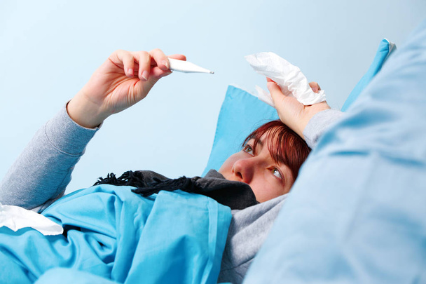 Foto einer kranken Frau mit Thermometer auf dem Bett liegend. - Foto, Bild