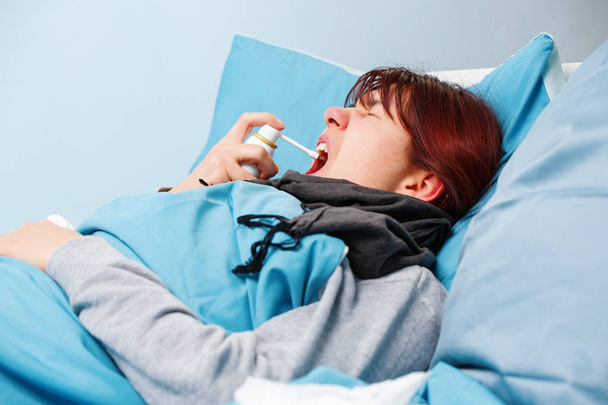 Εικόνα άρρωστο μελαχρινή χρησιμοποιώντας σπρέι λαιμό ξαπλωμένη στο κρεβάτι . - Φωτογραφία, εικόνα