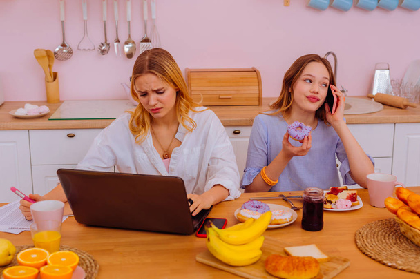 Teenage sibling speaking by phone and eating near working sister - Foto, imagen