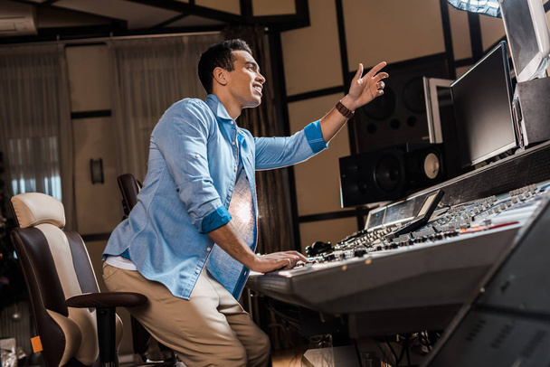 handsome mixed race musician gesturing while working at mixing console - Foto, Imagem