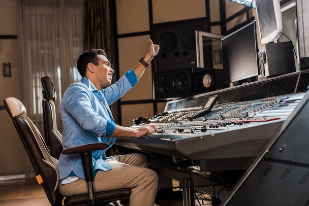 smiling mixed race sound producer showing thumb up while working at mixing console - Photo, Image