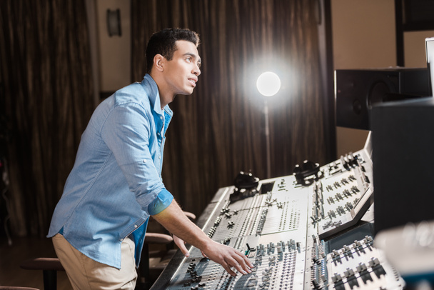 attentive mixed race sound producer working at mixing console in recording studio - Photo, Image