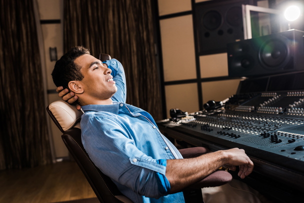 producteur sonore mixte souriant relaxant dans une chaise de bureau dans un studio d'enregistrement
 - Photo, image