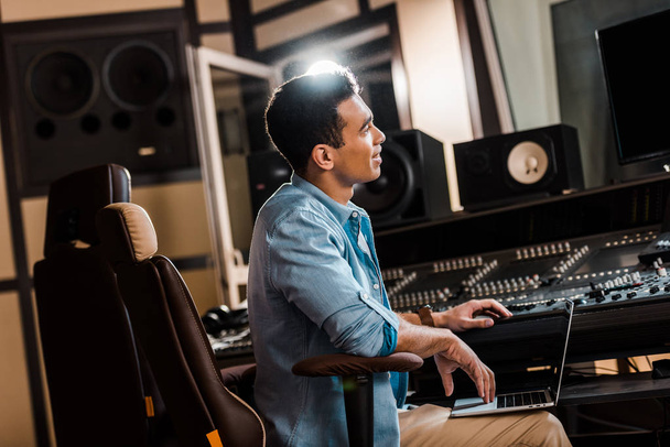 handsome smiling mixed race sound producer working in recording studio at mixing console - Foto, Imagen