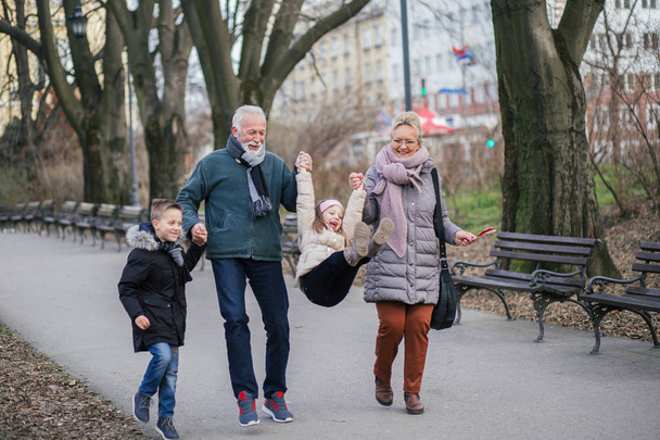 Isovanhemmat hauskaa lastenlastensa kanssa kaupungin puistossa
. - Valokuva, kuva