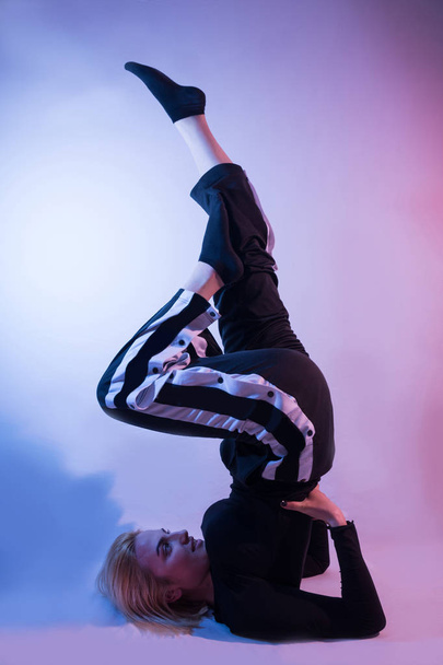 Nuori tyttö jalat ilmassa ja urheilu verryttelypuvut osoittaa hänen voimistelu taitoja värikäs tausta ja studio punainen ja sininen valot. Matala näppäinasetukset
 - Valokuva, kuva